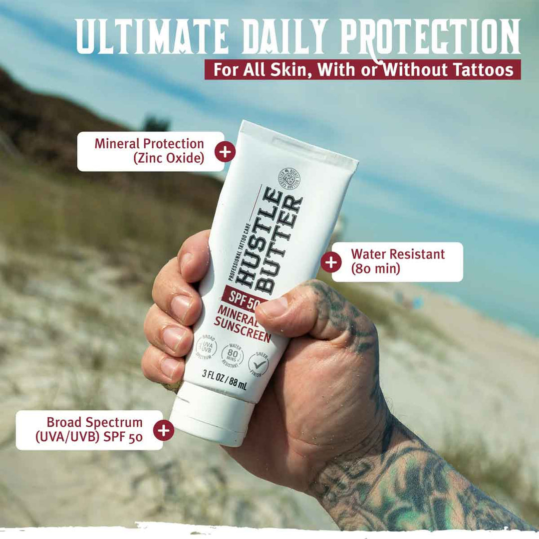 Hand holding a tube of Hustle Butter sunscreen with beach background