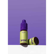Brovi One e-liquid bottle in 'warm light brown' flavor, featuring a lime green label and purple cap, shown standing next to its matching purple cap on a white surface against a solid purple background.