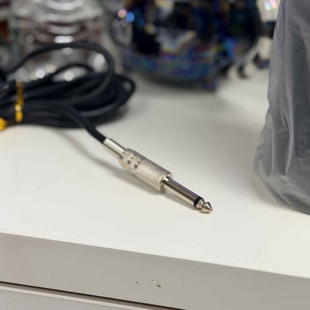 Audio cable connector for a tattoo pedal on a white surface with blurred background