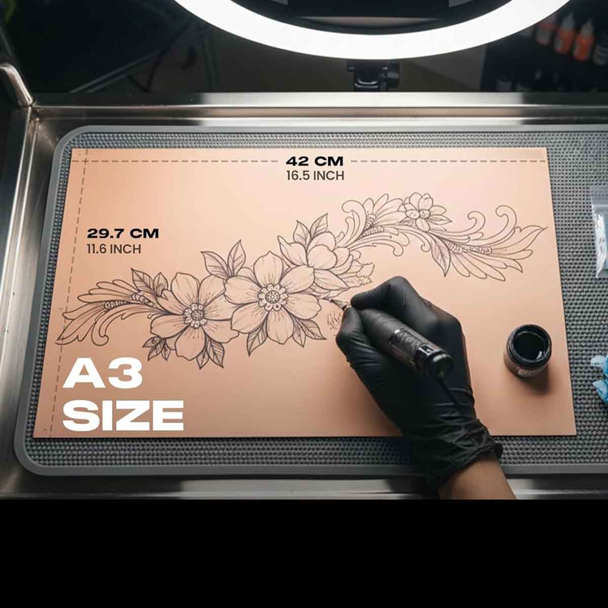 Person drawing floral designs on a large A3 size leather mat with a pen.